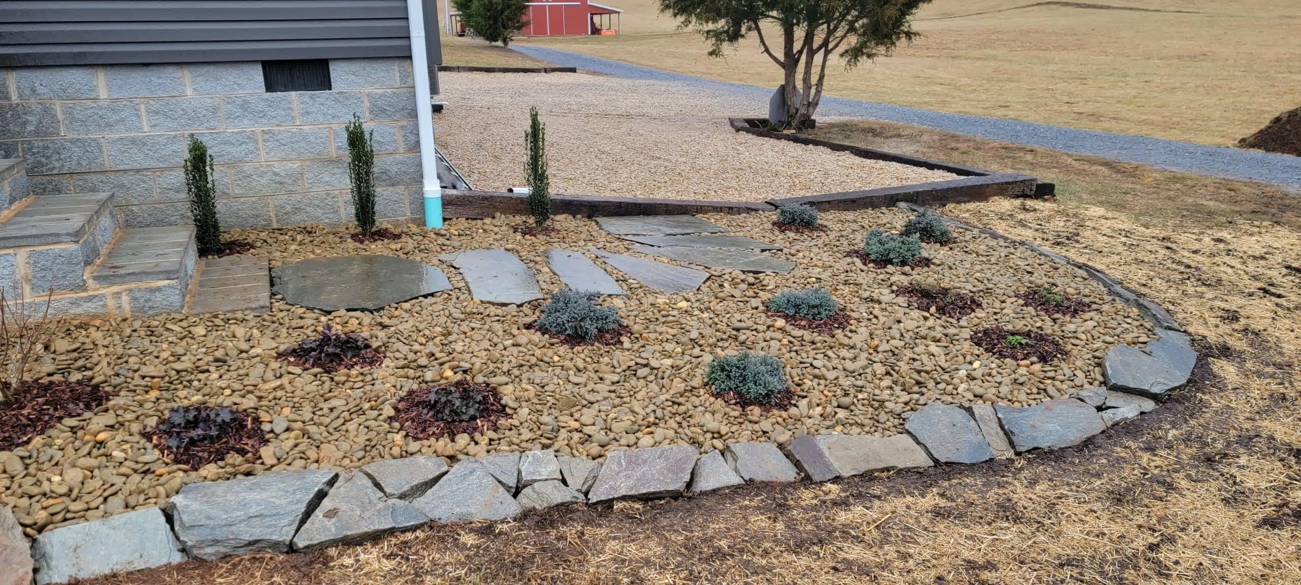 Drought-resistant landscape with stepping stones, decorative river rock, and small shrubs arranged neatly along a home’s foundation.