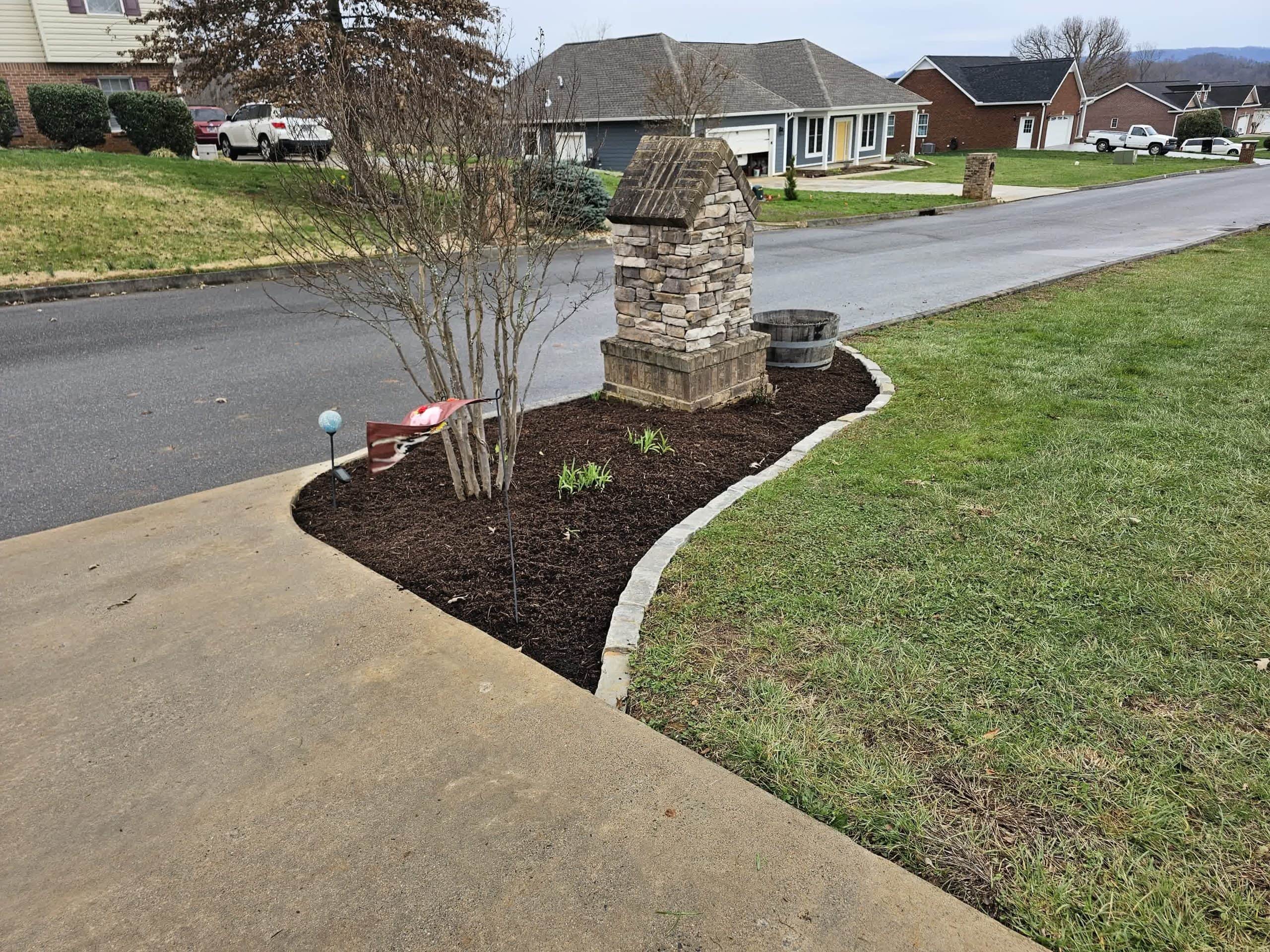 Mulched flower bed with a stone mailbox and dormant shrubs, adding structure and definition to a suburban front yard.