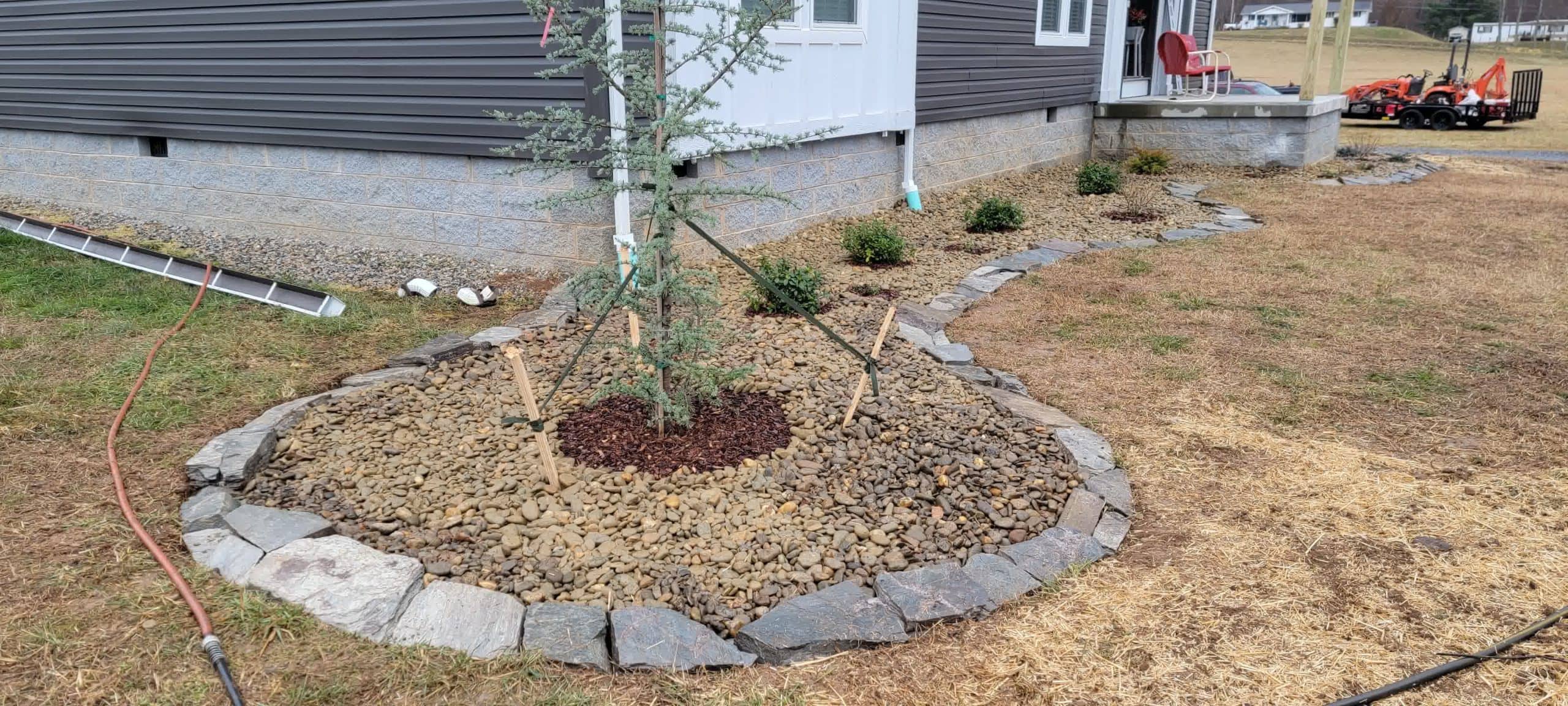 Newly planted tree with rock mulch and a stone border, part of a sustainable landscape design for erosion control and drainage.	