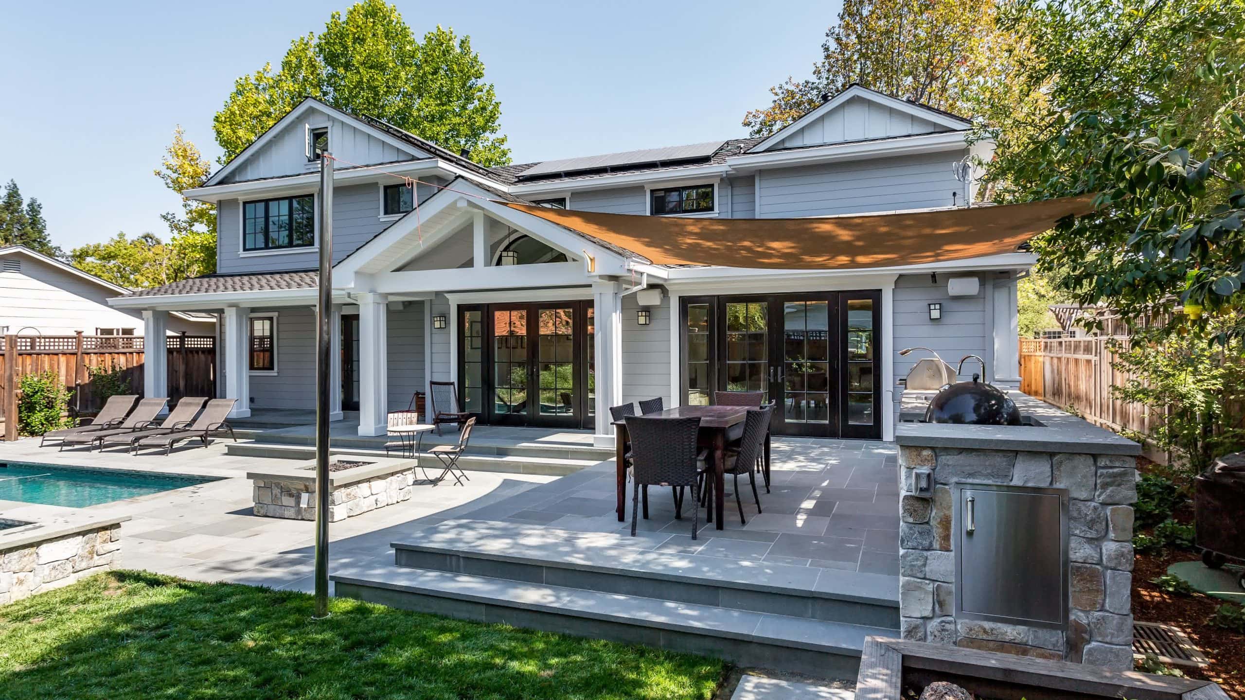 Modern backyard patio with a shaded dining area, outdoor kitchen, and a swimming pool, designed for stylish outdoor living.
