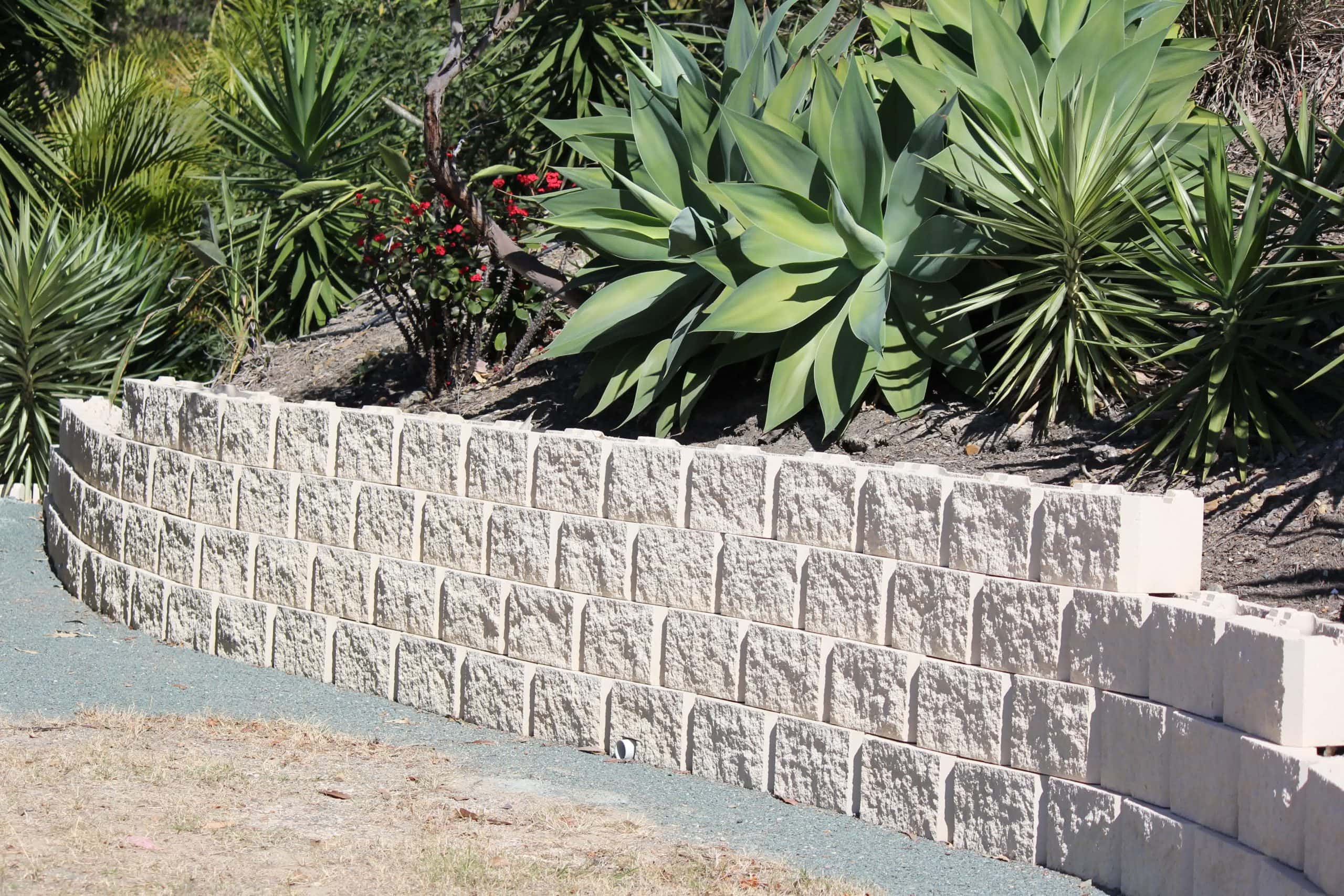 Curved retaining wall with textured stone blocks, surrounded by drought-resistant plants and succulents for erosion management.