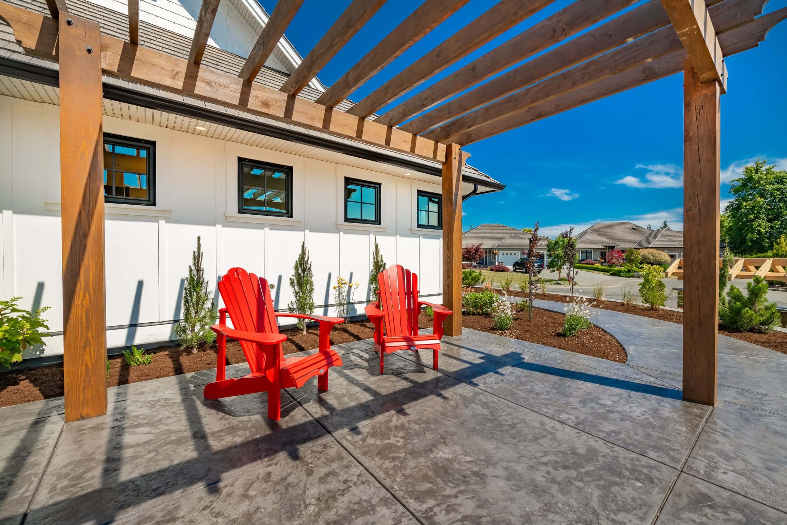 Outdoor pergola with two red Adirondack chairs on a stamped concrete patio, offering a relaxing backyard seating area.