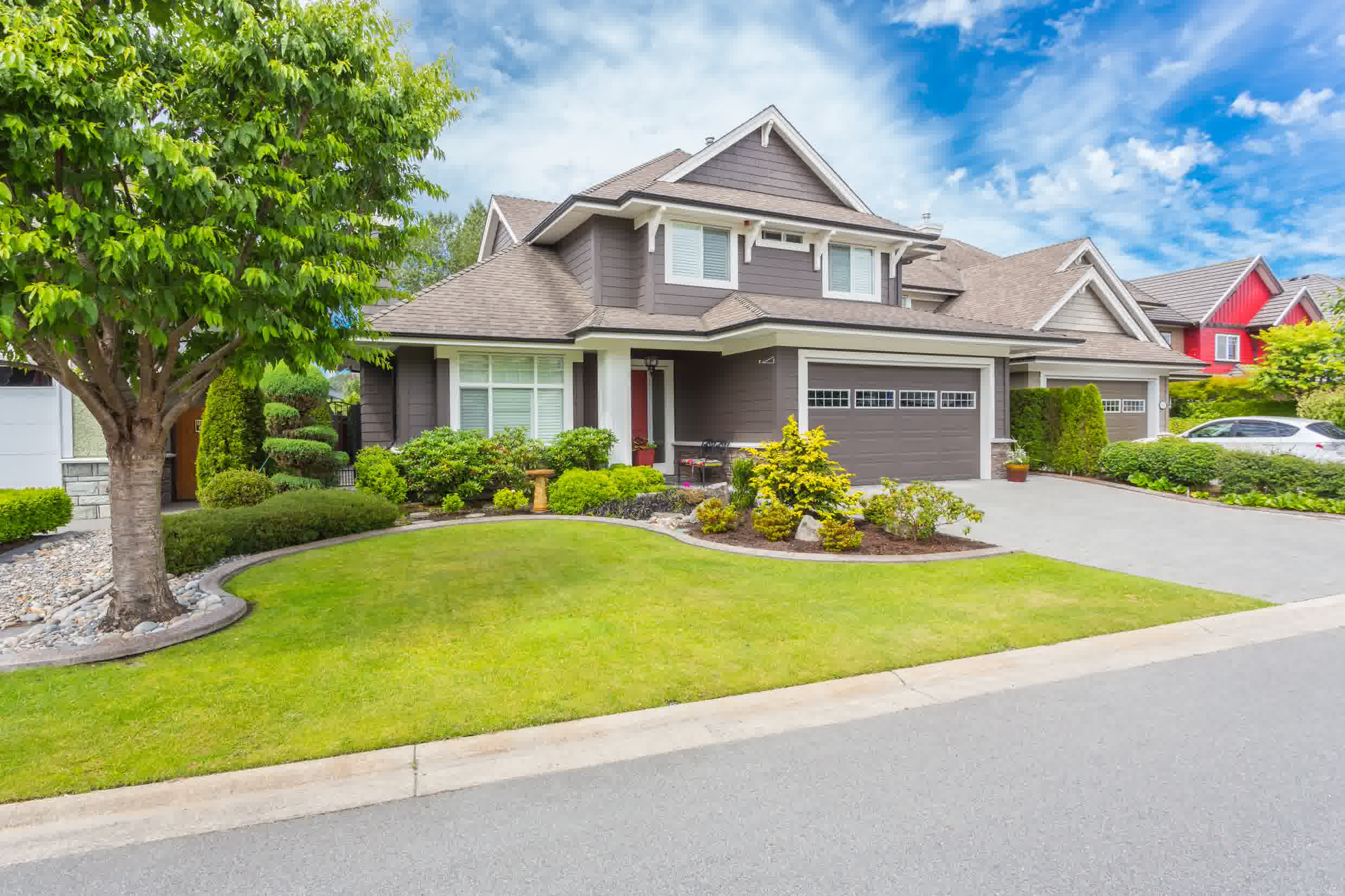Modern home with landscaped front yard, vibrant green lawn, and colorful shrubs under a clear blue sky.